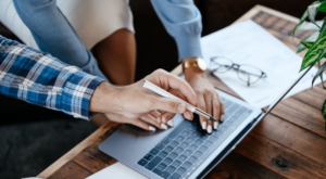 Two colleagues reviewing documents and a laptop while deciding whether to outsource IT